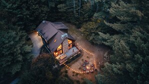 An aerial view of a cabin surrounded by dense forest, with a deck and outdoor seating area.