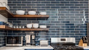 A modern kitchen with blue-tiled backsplash, stainless steel appliances, and wooden shelves.