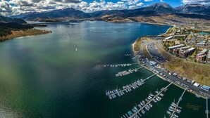 Vista aérea de un pueblo costero con un puerto deportivo, barcos y montañas al fondo.