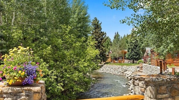Un puente de piedra sobre un río con pasarela de madera, rodeado de exuberante vegetación y cabañas de madera.