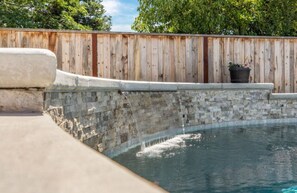 A swimming pool with a stone wall and a wooden fence in the background.