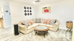 Un salón con un sofá seccional color beige, una mesa de centro redonda, un tapete estampado y una pared decorada con elementos circulares.