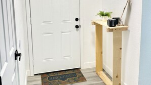 Un pasillo con una puerta blanca, una consola de madera con una planta pequeña y un felpudo.