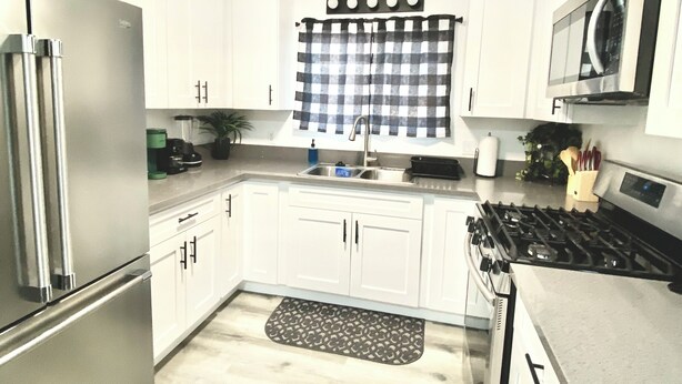 Cocina moderna con armarios blancos, electrodomésticos de acero inoxidable, un valance de ventana a cuadros y una alfombra estampada.