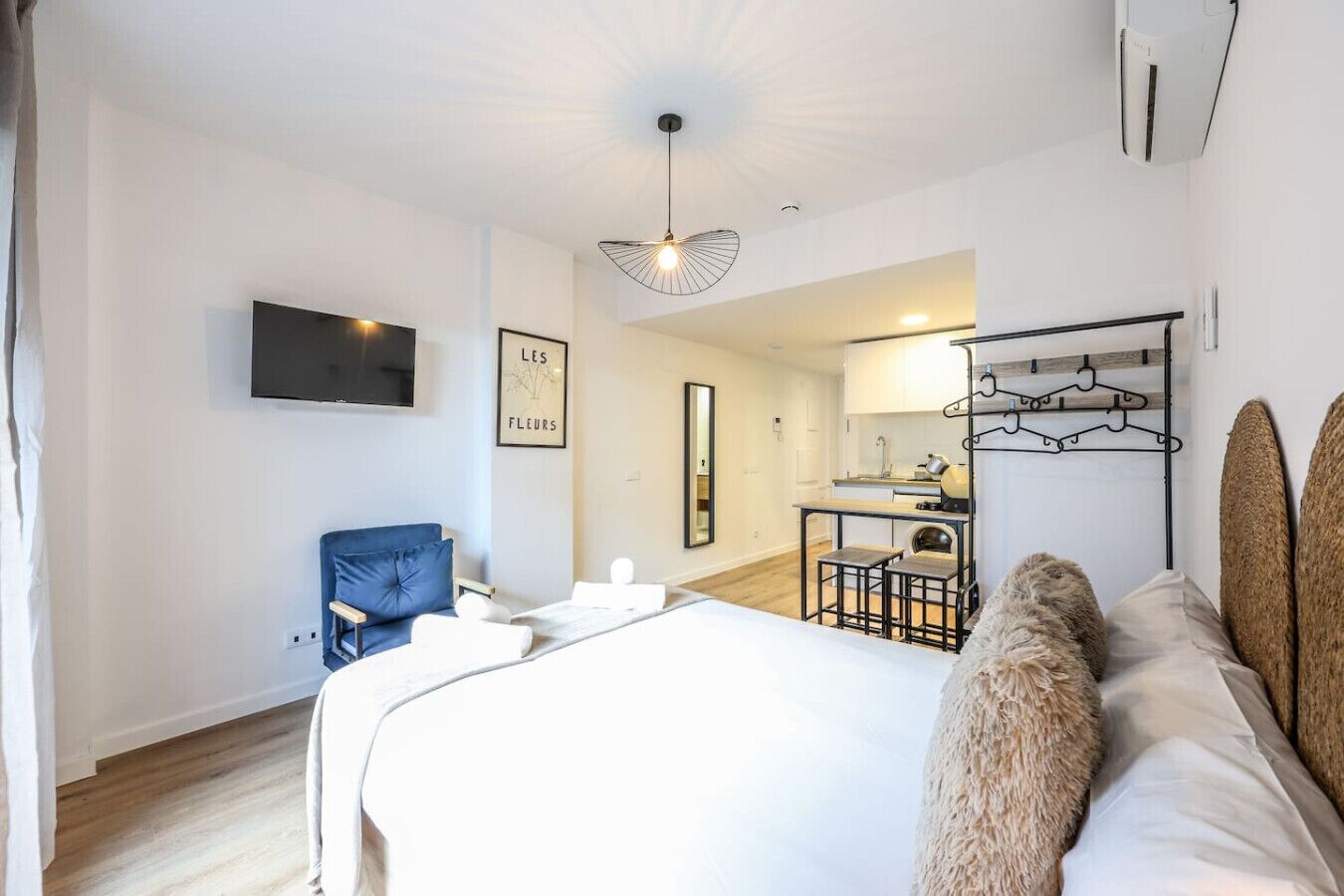 Una habitación de hotel moderna con una cama grande, un escritorio con dos sillas, una lámpara colgante y un televisor de pared.
