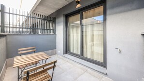 Ein Balkon mit Holztisch und -bänken, einem Metallzaun und einer Schiebeglastür.