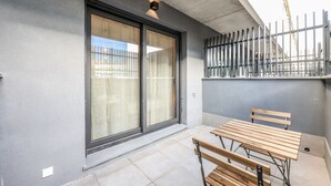 A modern outdoor patio with a sliding glass door, a metal fence, and a wooden bench. - Elegant Studio with Private Terrace by RentitUP (San Sebastián de los Reyes)