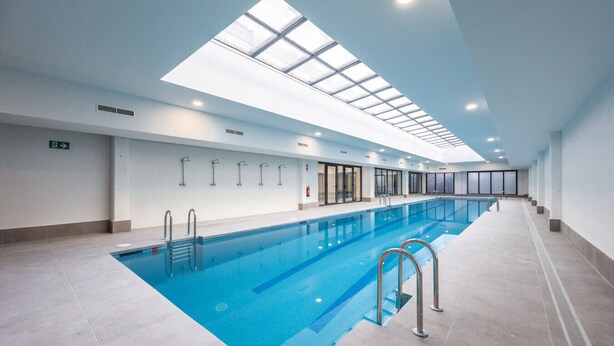 A large indoor swimming pool with clear blue water, surrounded by a tiled floor and walls, and a skylight above. - Elegant Studio with Private Terrace by RentitUP (San Sebastián de los Reyes)