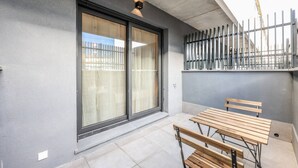 En balkon med træbænk, skydedør i glas og metalhegn.