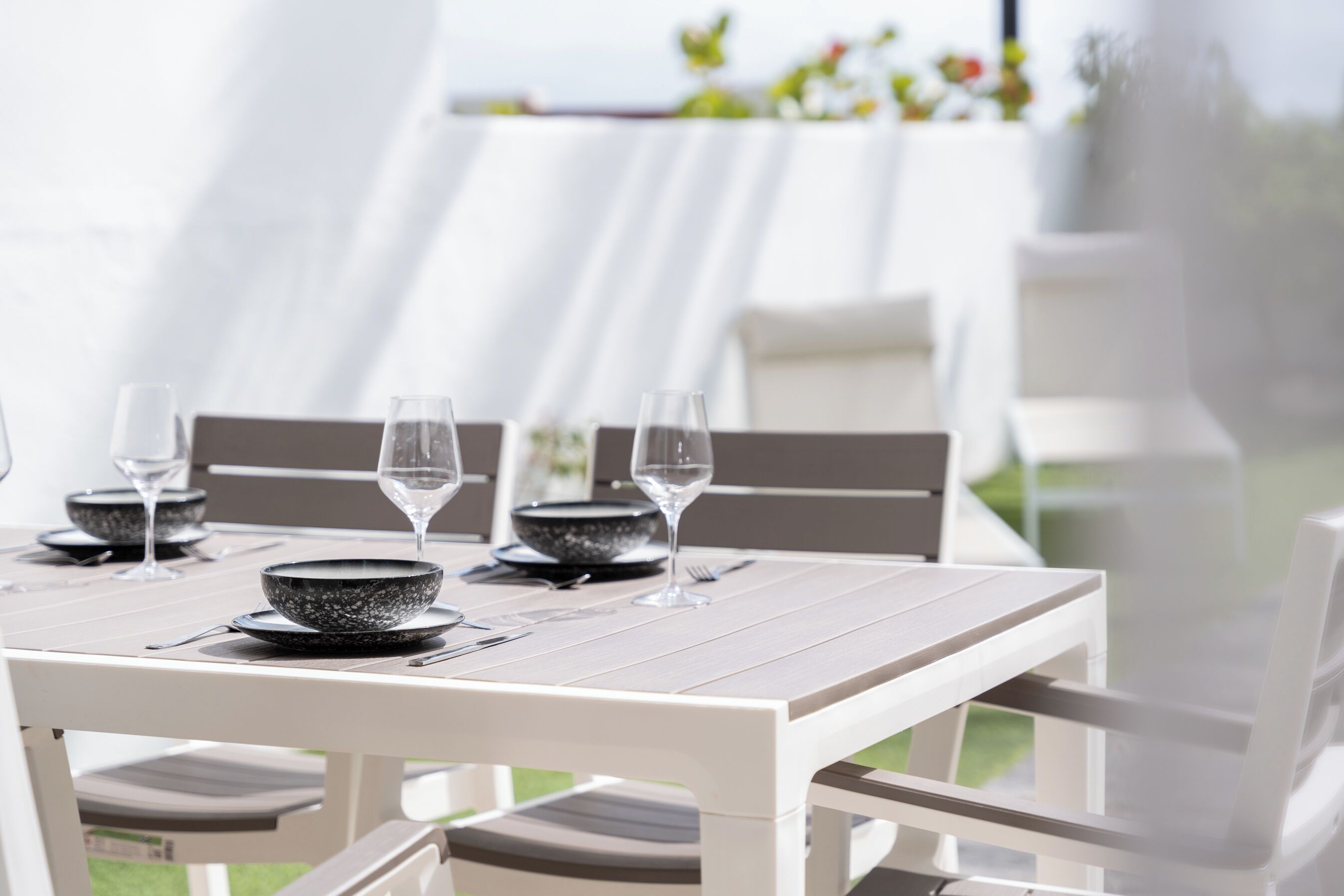 A dining table set with bowls and wine glasses, surrounded by white chairs.