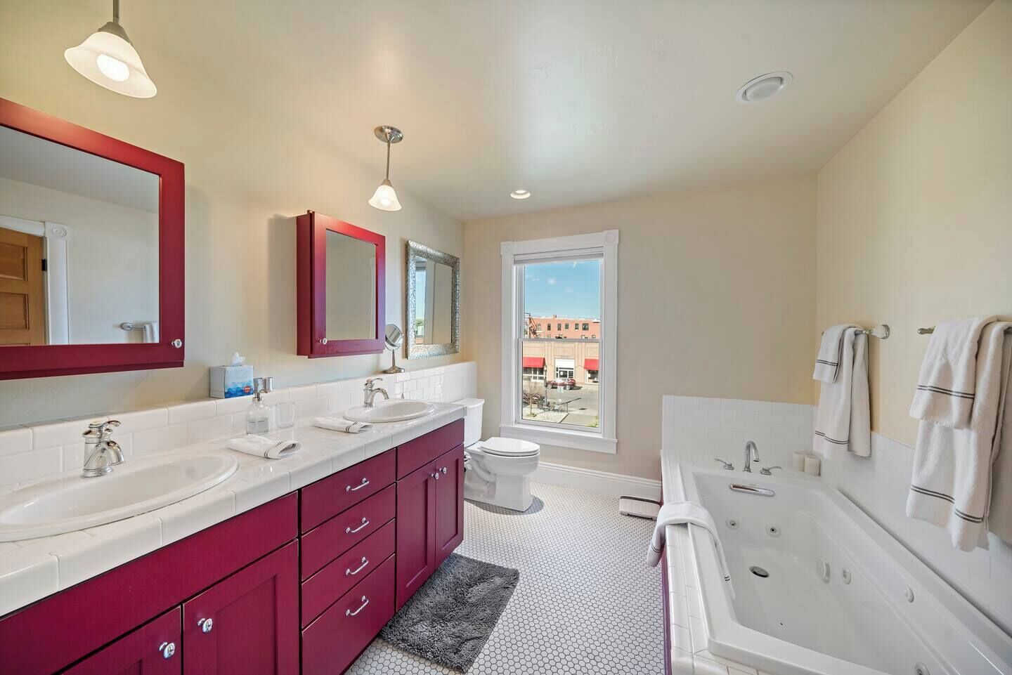 A modern bathroom with two sinks, a large mirror, a window, and a bathtub.