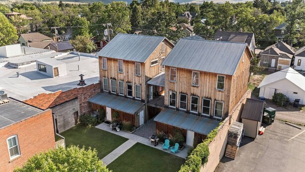 A two-story wooden house with a flat roof, a front porch, and a small backyard with a lawn and two chairs. - Serendipity House: Historic Downtown Livingston Loft (Livingston)