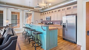 A modern kitchen with a central island, bar stools, stainless steel appliances, and wooden cabinets. - Serendipity House: Historic Downtown Livingston Loft (Livingston)