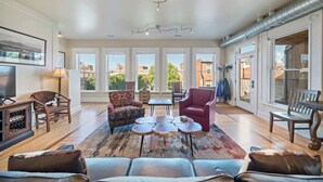 A spacious living room with a large window, a fireplace, and a dining area. - Serendipity House: Historic Downtown Livingston Loft (Livingston)