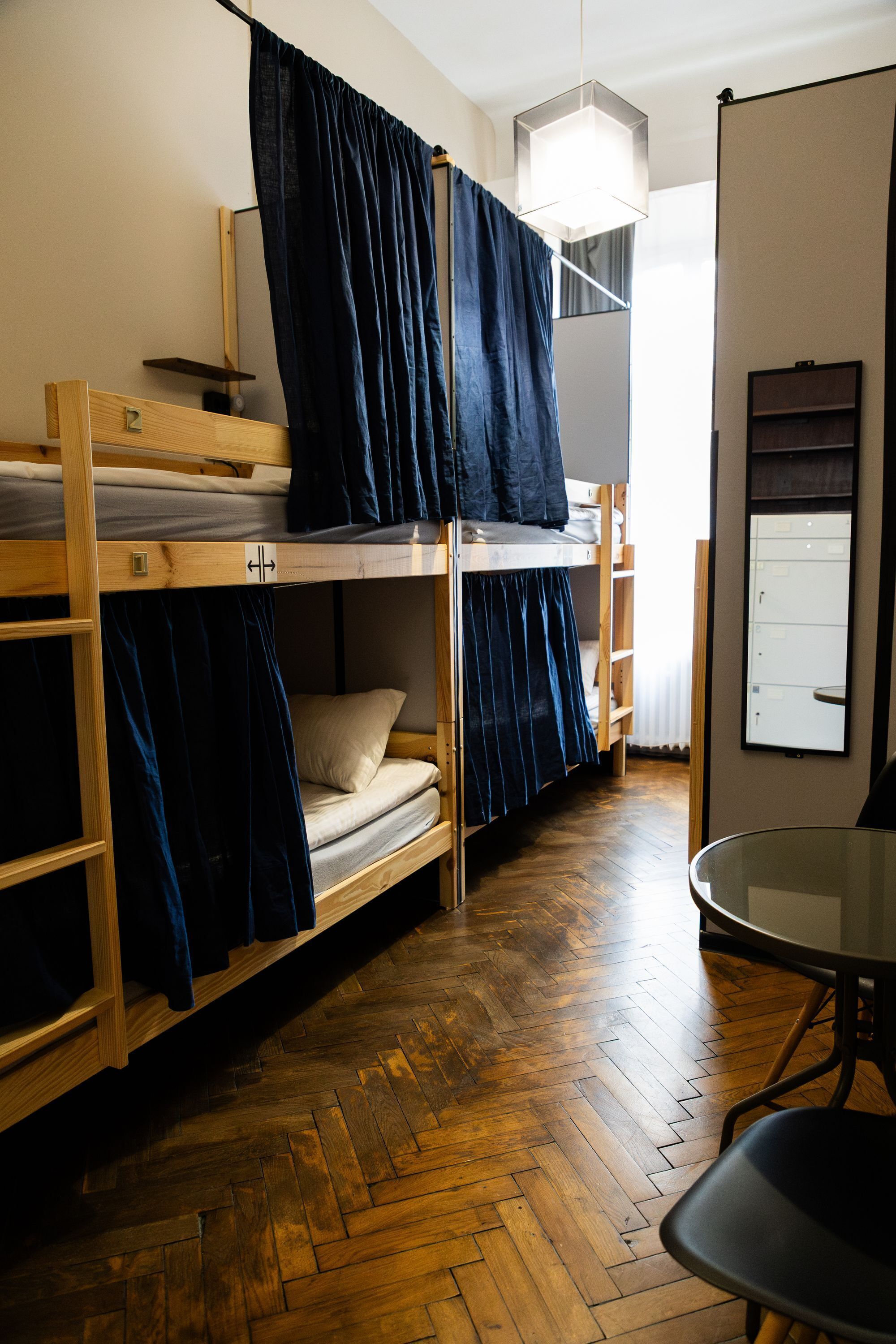 Habitación tipo dormitorio con literas, suelo de madera, una mesa y un armario fijado a la pared.