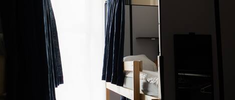 Habitación pequeña con una litera, una lámpara colgante y una ventana con cortinas.