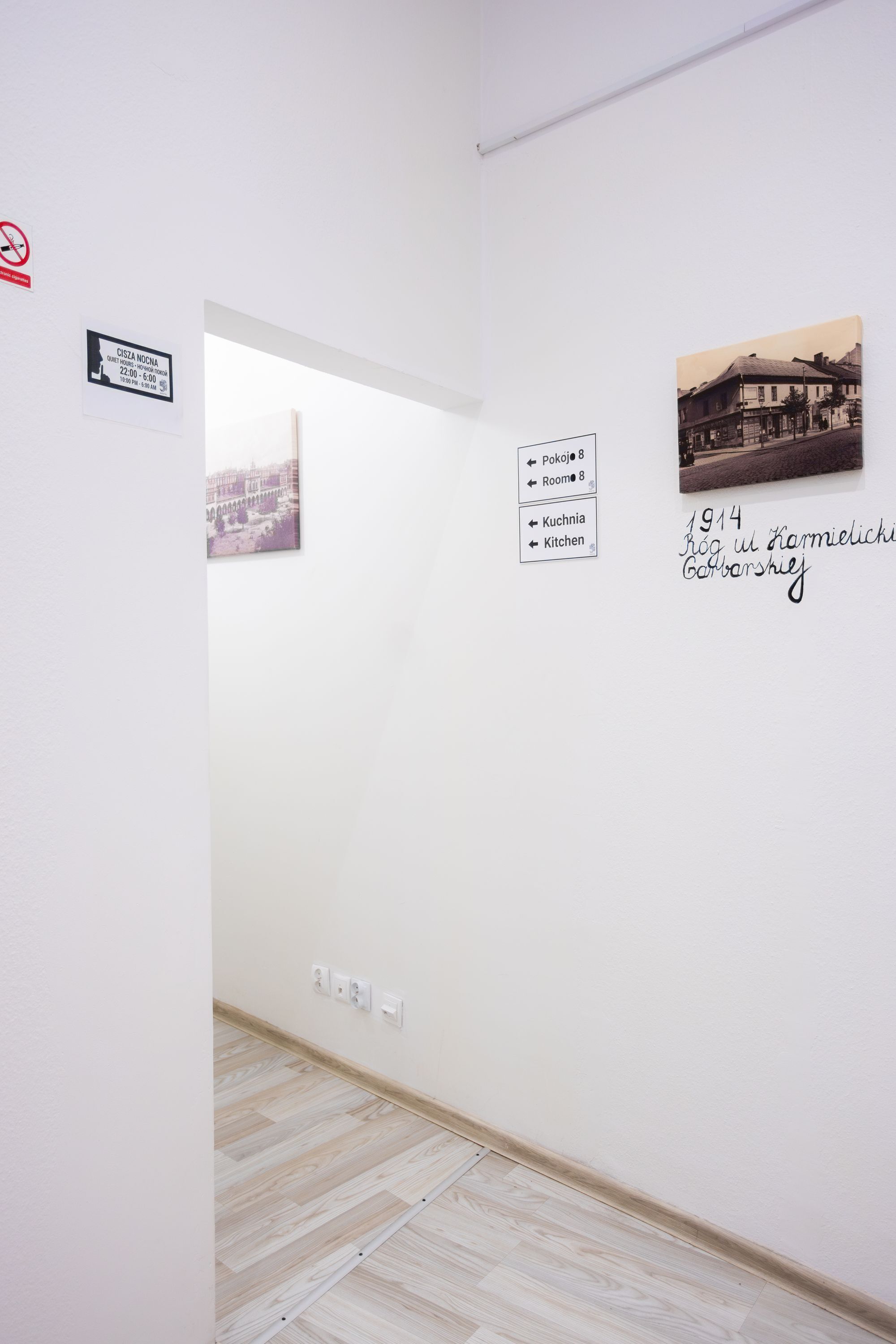 A hallway with a white wall, a framed photograph, and directional signs.