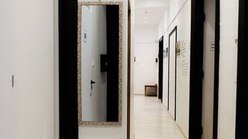 A hallway with a mirror, wooden flooring, and doors leading to rooms.
