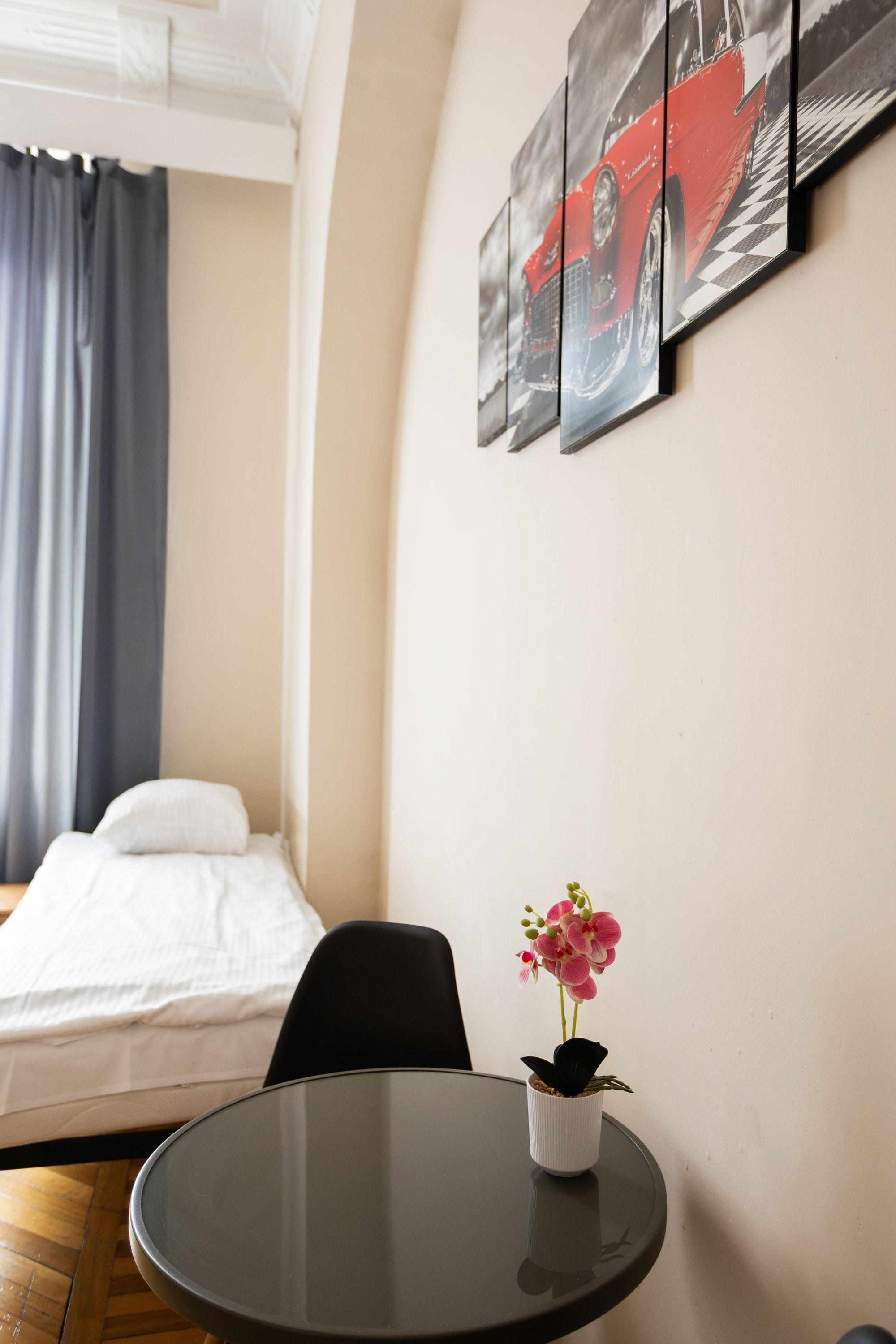 A hotel room with a bed, a small table with a potted orchid, and a wall with a car-themed artwork.