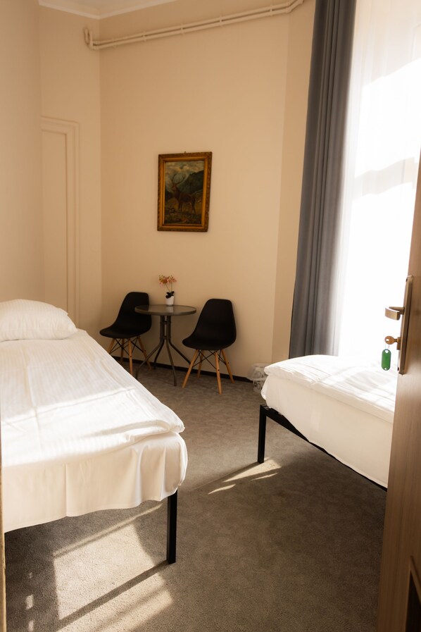 Habitación de hotel con dos camas, una mesita con sillas, un cuadro en la pared y una ventana con cortinas.