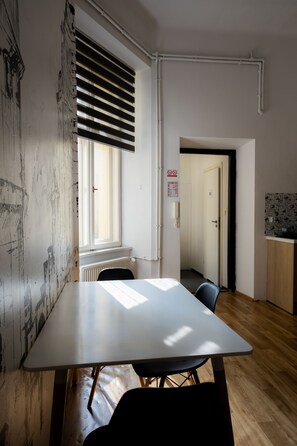 A room with a large table, a window with blinds, a radiator, and a door leading to another room. - FiveHostel (Kraków)