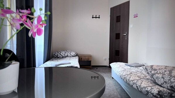 A bedroom with a bed, a bedside table, a dresser, and a window with curtains. - FiveHostel (Kraków)