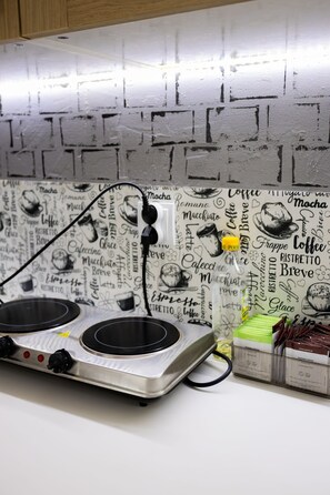 A kitchen with a modern induction cooktop and a coffee-themed backsplash. - FiveHostel (Kraków)