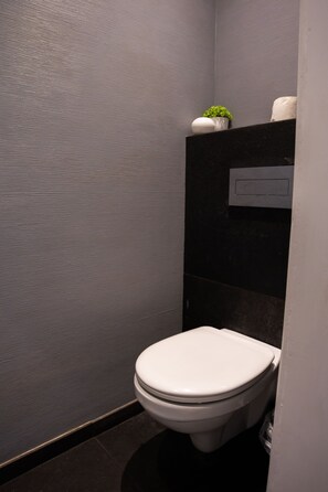 A modern bathroom with a toilet, a small potted plant, and a towel dispenser. - FiveHostel (Kraków)