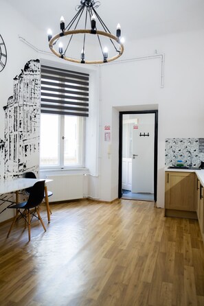A modern kitchen with a wooden floor, a dining area with a table and chairs, and a large window with blinds. - FiveHostel (Kraków)