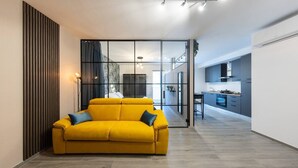 A modern living room with a yellow sofa, a glass partition, and a kitchen in the background. - Urban Chic Luxury Suite Apartments (Roma)