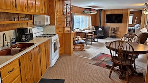 Una cocina acogedora de estilo cabaña con armarios de madera, una estufa y un comedor con sillas y mesa de madera.