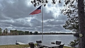 Un patio junto al lago con un asta de bandera, una mesa y sillas.