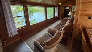 A cabin with a long wooden interior, large windows overlooking a lake, a sofa, and a lamp. - Shady Rest Cabin #1, Sunset Views, Beach, Pets Welcome, Swimming, Firepit (Rhinelander)