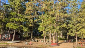 A lakeside area with trees, a dock, and outdoor seating by the water. - Shady Rest Cabin #1, Sunset Views, Beach, Pets Welcome, Swimming, Firepit (Rhinelander)