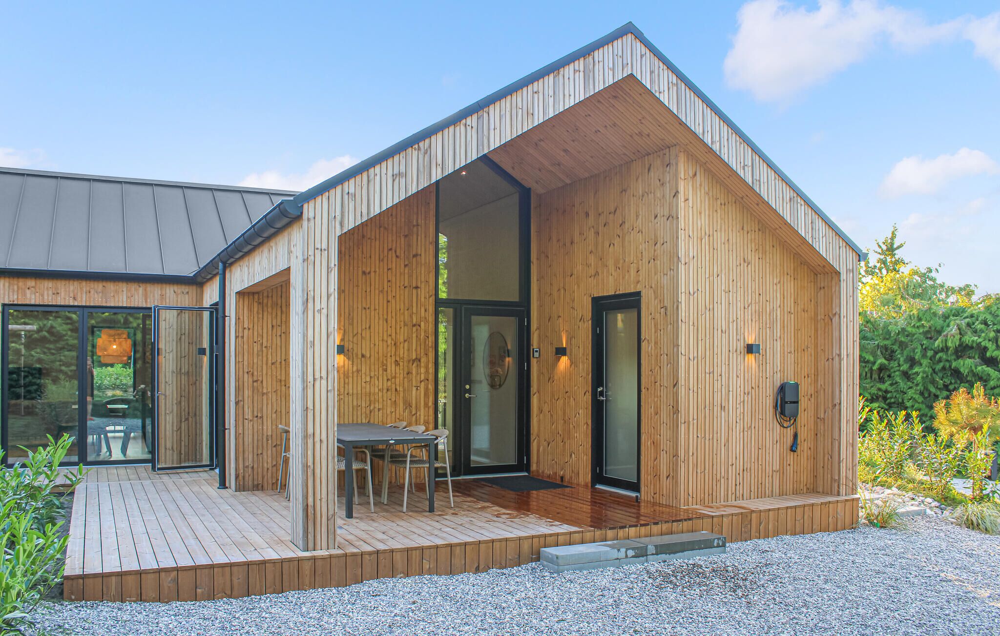 Une maison moderne en bois, dotée d’une terrasse, de grandes portes vitrées et d’un petit espace de détente extérieur.
