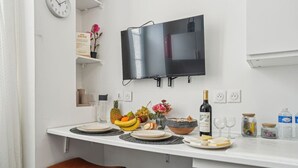 Een moderne keuken met een wit aanrecht, een zwart scherm aan de muur en een eethoek met twee bruine krukken.