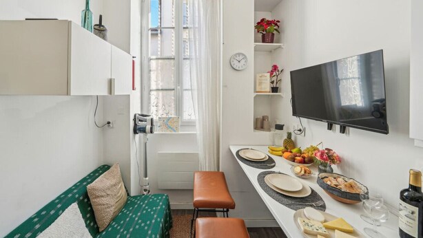 Een compacte keuken met een eethoek, een aan de muur bevestigde televisie en een raam met gordijnen.