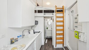 Een kleine keuken met een ingebouwde kookplaat, een spoelbak en een ladder die naar een kleine badkamer leidt.