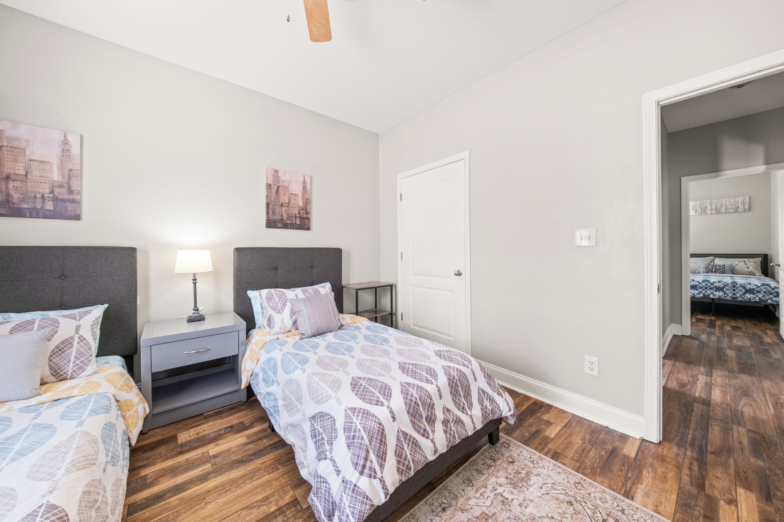 Une chambre avec deux lits, une table de chevet, une lampe et une porte.