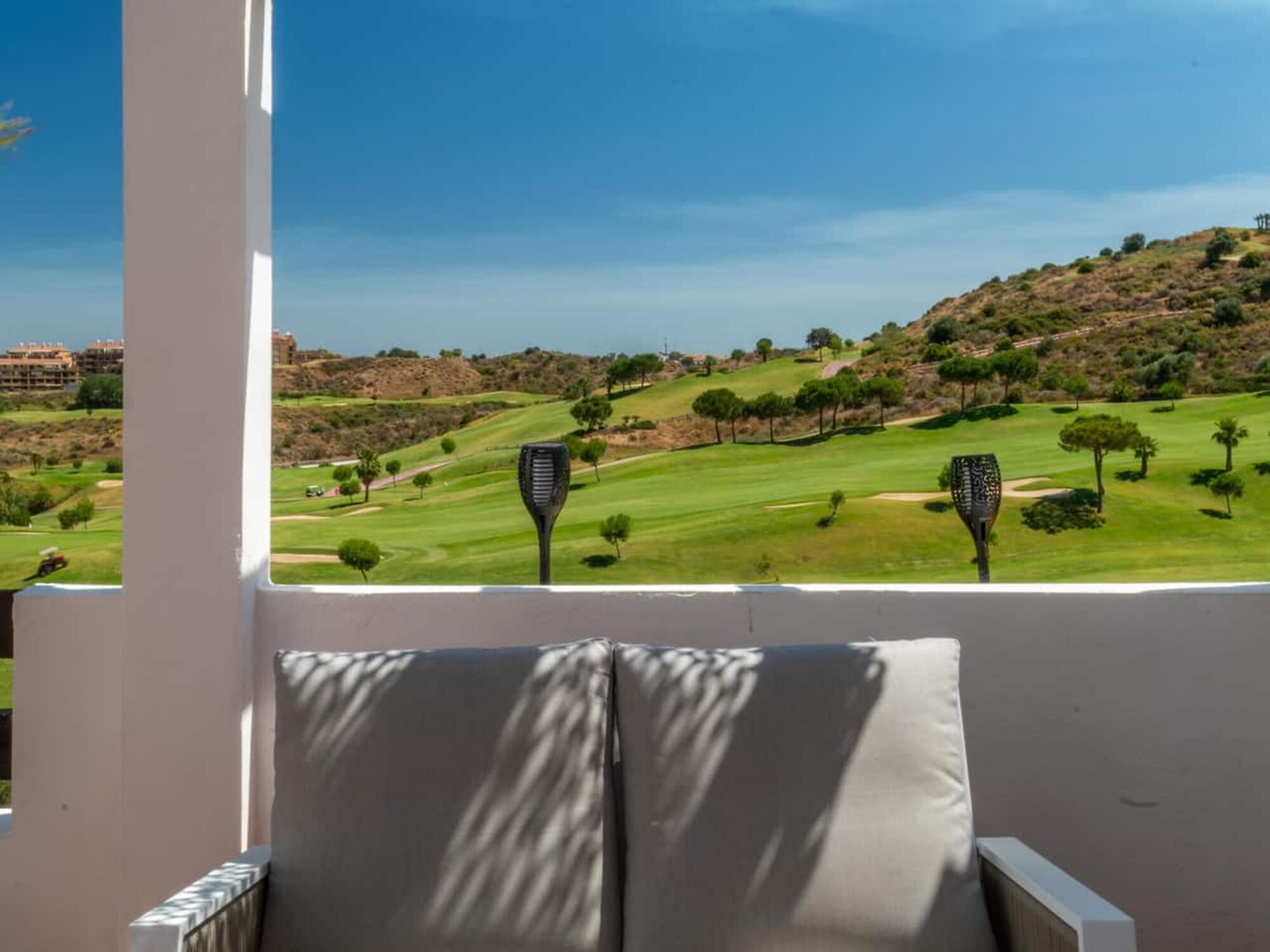 A balcony with a view of a golf course, a chair, and a decorative lamp.