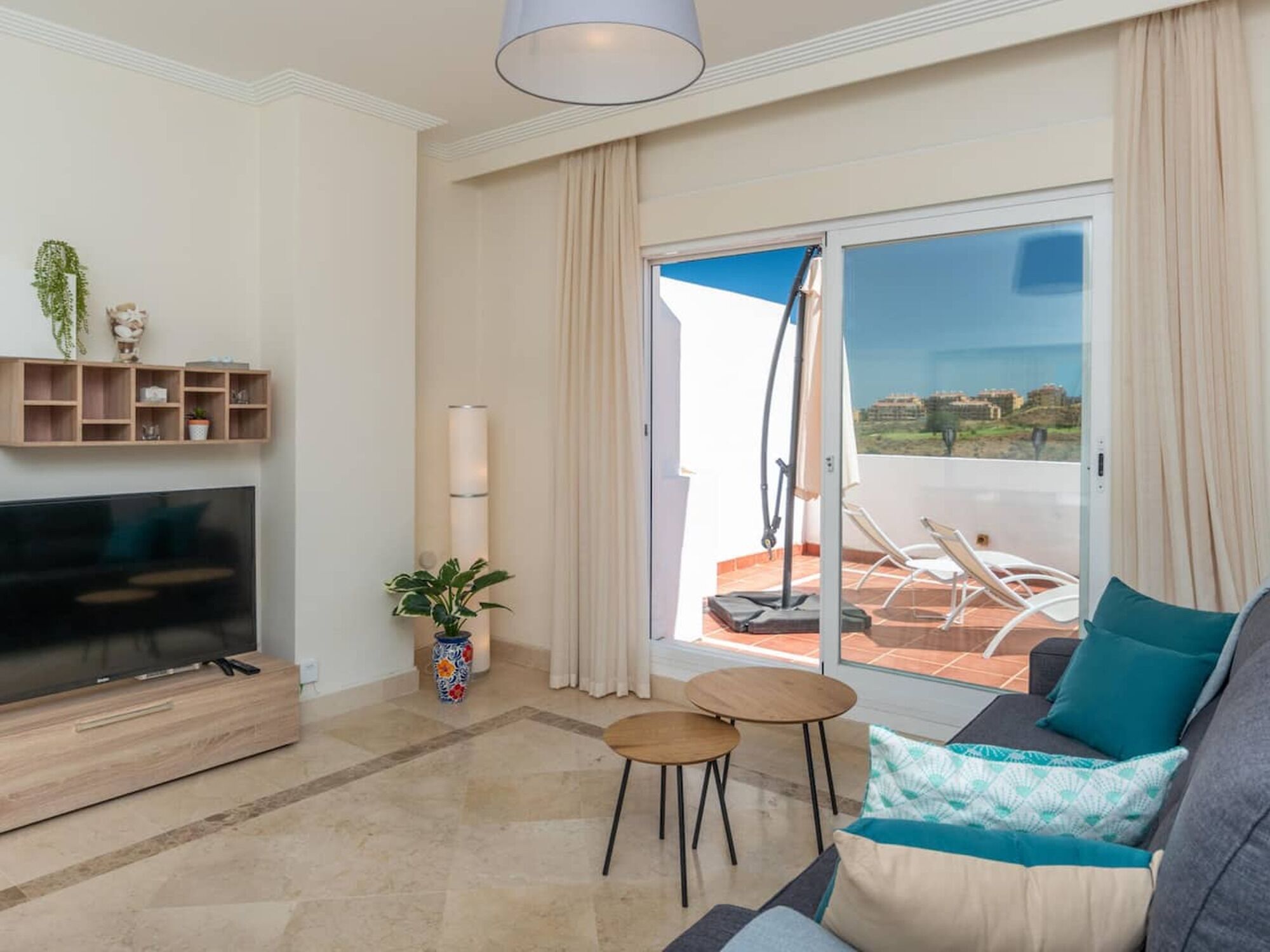 Un salon moderne doté d’un téléviseur à écran plat, d’un canapé, d’une petite table, d’une plante en pot et d’un balcon avec vue.