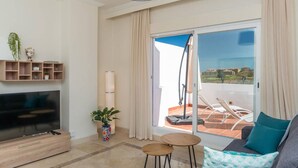 Een moderne woonkamer met een flatscreentelevisie, een bank, een bijzettafeltje, een kamerplant en een balkon met uitzicht.