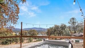 A hot tub with a control panel, surrounded by a wooden fence, with a view of a mountainous landscape and trees in the background.