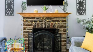 A living room with a stone fireplace, a flat-screen TV mounted above it, and decorative pineapples on the mantel. - Spacious 5-bedroom Pineapple House in wonderful Pikesville/10PPL/Pets/ WiFi (Pikesville)