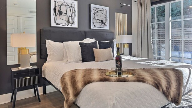 A modern bedroom with a large bed, a nightstand, a lamp, and artwork on the wall. - Upscale suite w/ pool & extra large balcony (Birmingham)