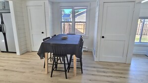 Un comedor con mesa y sillas, un refrigerador y una ventana con vista al patio trasero.