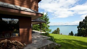 Una casa de madera con un patio de piedra, vista a un lago y una pila de leña.