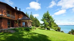 Una casa moderna con un amplio porche, vistas al lago y un césped cuidado.