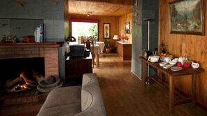 Una sala de estar acogedora con chimenea, un sofá, una zona de comedor con sillas y una encimera de cocina con varios objetos.