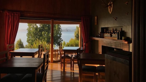 Una habitación acogedora con un amplio ventanal con vistas a un lago, muebles de madera y una chimenea.